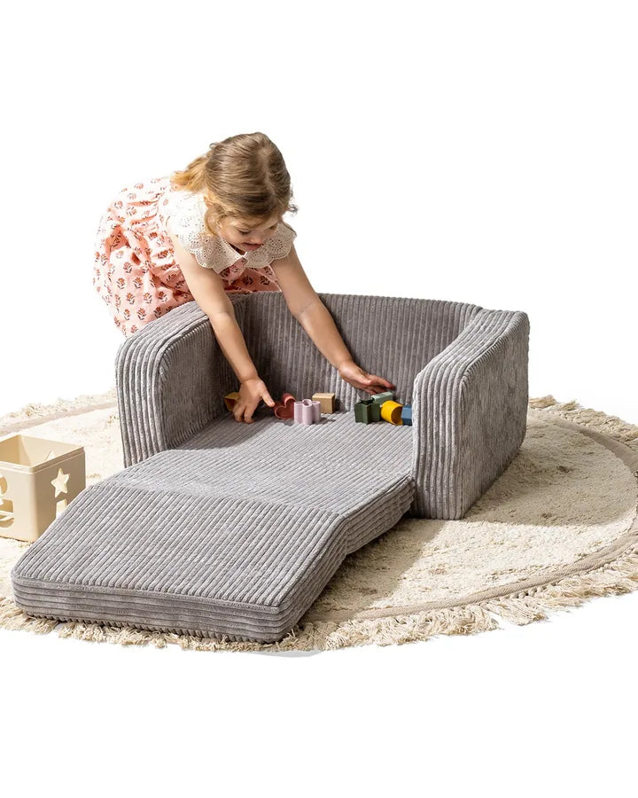 Dziewczynka bawi się na rozłożonym foteliku Lumi Chair Corduroy w kolorze Pebble