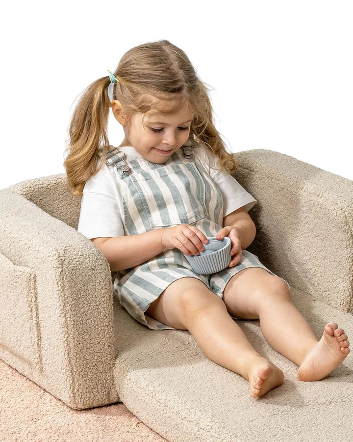 Dziewczynka leży na rozłożonym foteliku Lumi Chair Teddy w kolorze Light Beige