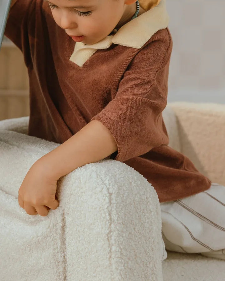Dziecko siedzi z książką na foteliku Lumi Chair Teddy w kolorze Soft Cream