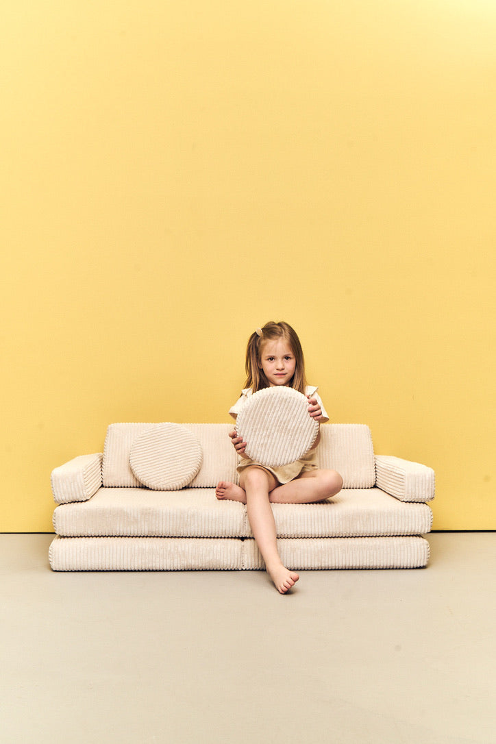 Dziecko siedzi na Play Sofa Pure Corduroy Mini w kolorze Vanilla z okrągłą poduchą