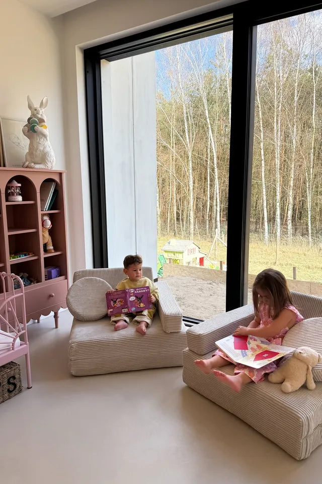 Dwoje dzieci czyta w siedziskach zbudowanych ze sztruksowej sofy do zabawy