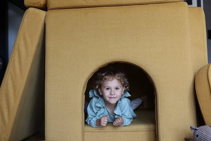 Dziecko leży w wejściu do zamku zbudowanego z Arches w kolorze Mustard