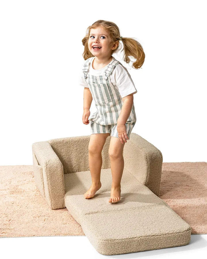 Dziewczynka stoi na rozłożonym foteliku Lumi Chair Teddy w kolorze Light Beige