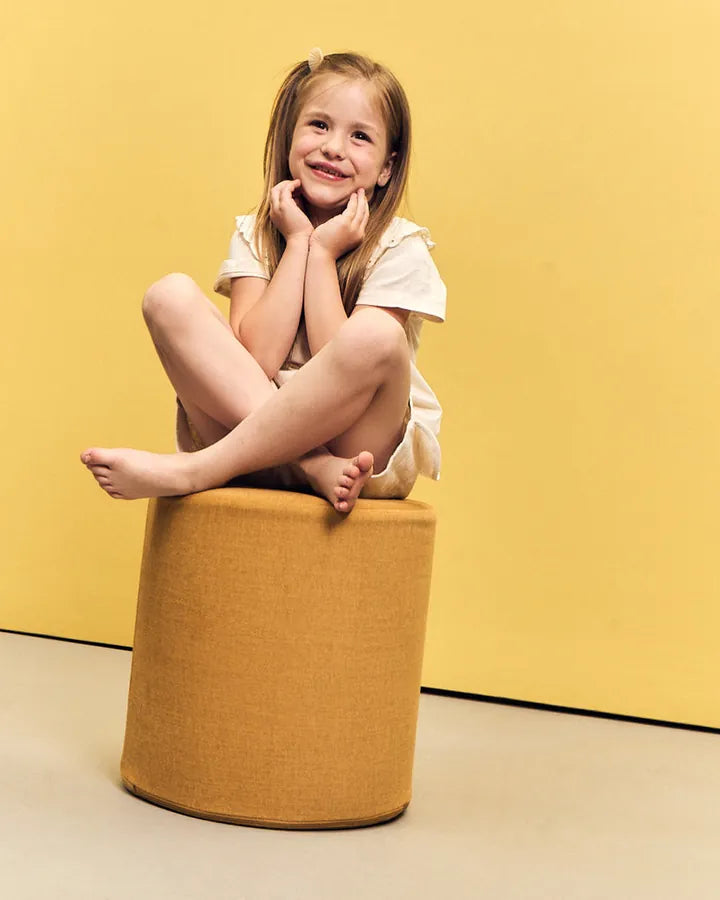Dziewczynka siedzi na pufie Shappy Pouf Ultra Plush w kolorze Mustard