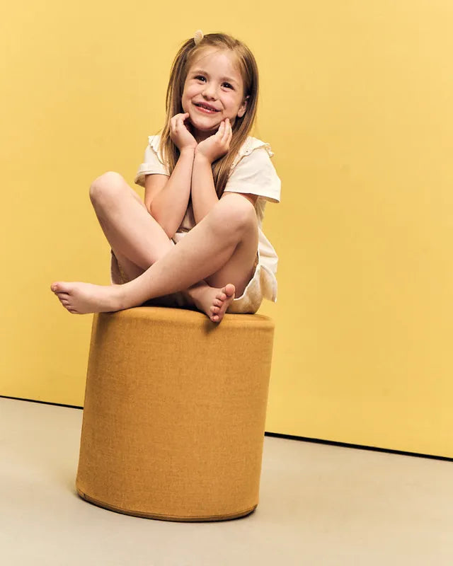Dziewczynka siedzi po turecku na pufie Shappy Pouf Ultra Plush w kolorze Mustard