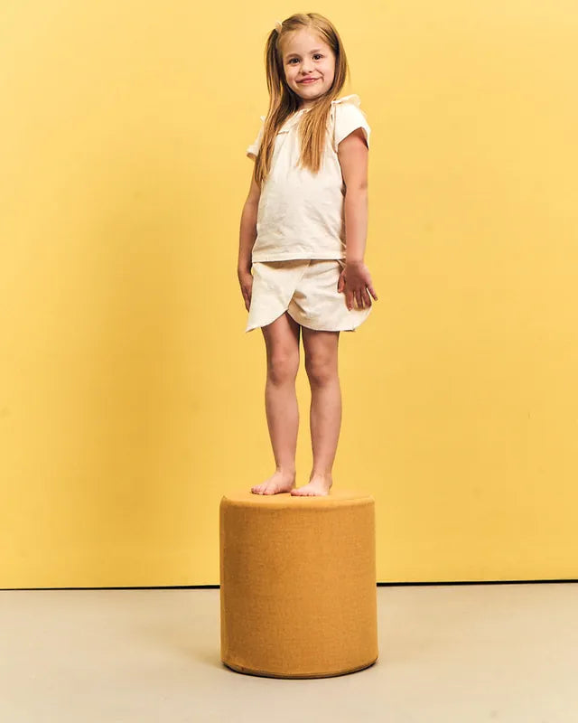 Dziewczynka stoi na pufie Shappy Pouf Ultra Plush w kolorze Mustard