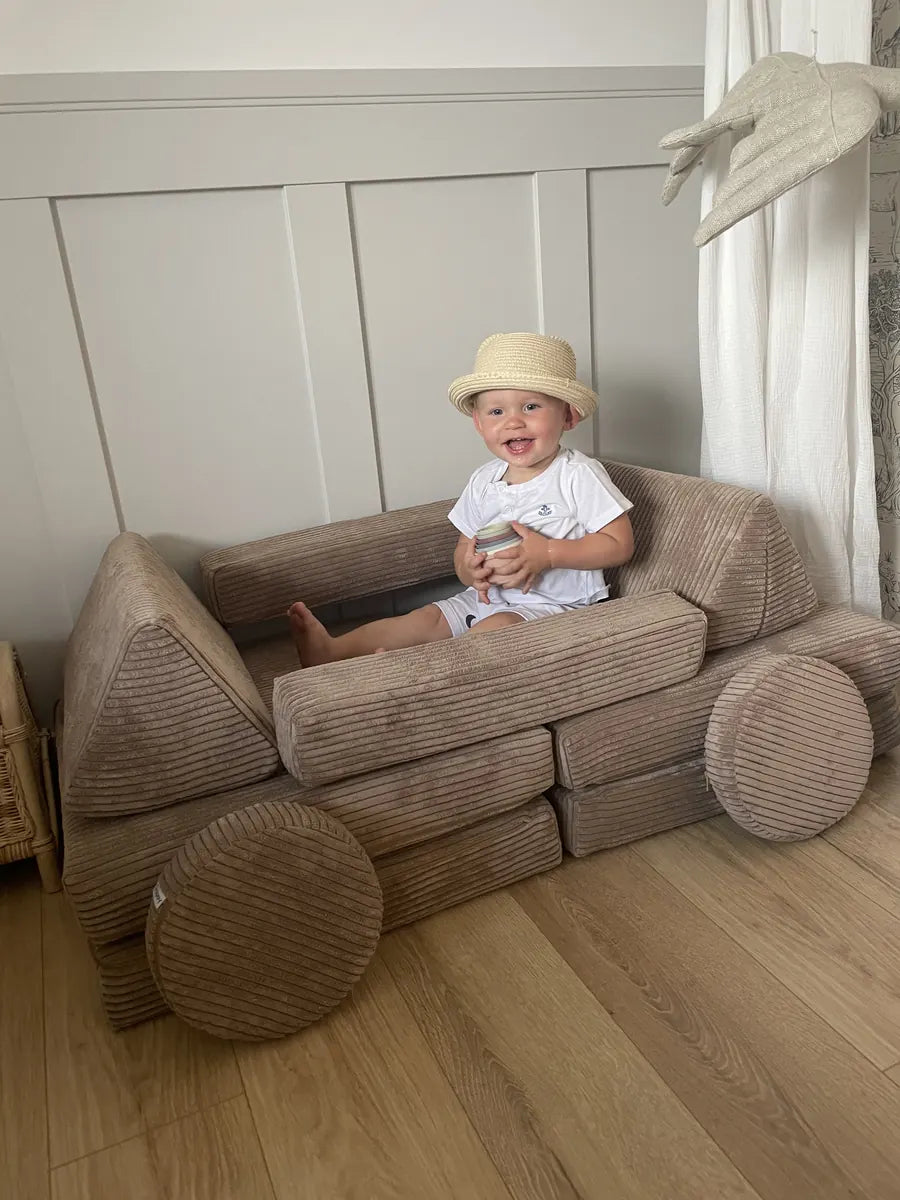 Maluch siedzi w samochodzie zbudowanym z Play Sofa Pure Corduroy Mini w kolorze Chocolate