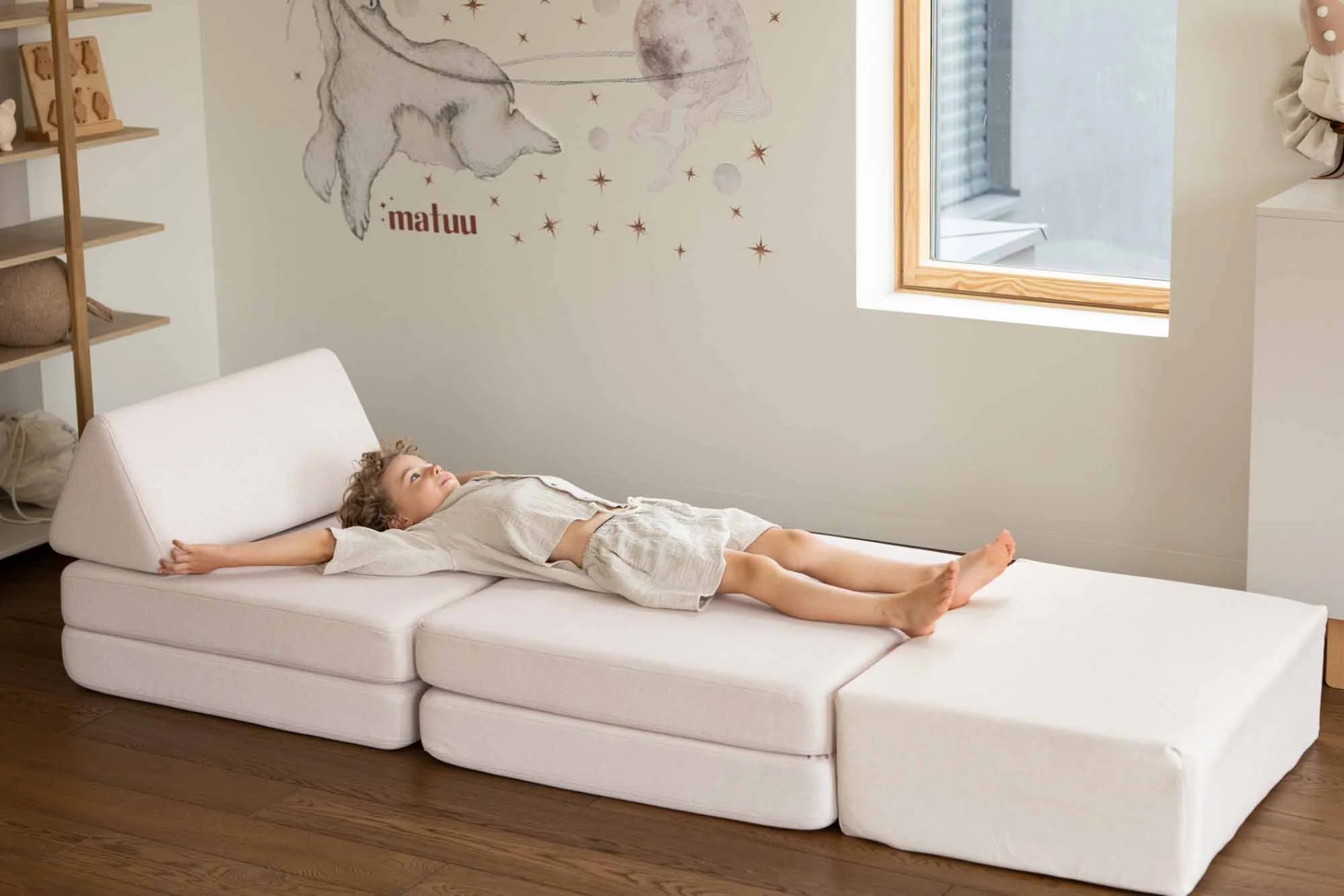 Chłopiec leży na Play Sofa Original w kolorze Soft Beige przedłużonej trampoliną