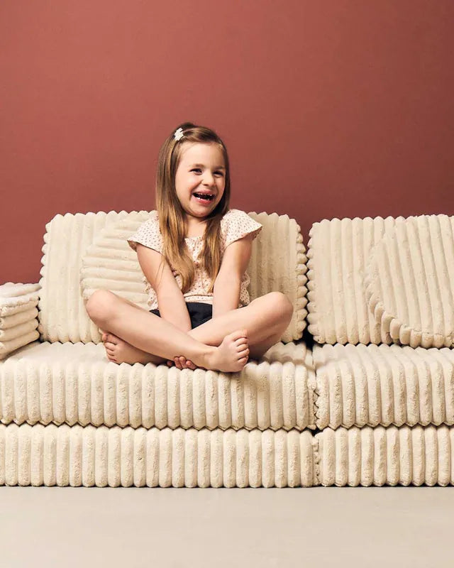 Dziewczynka siedzi na Play Sofa Pure Corduroy Waffle w kolorze Cream Beige