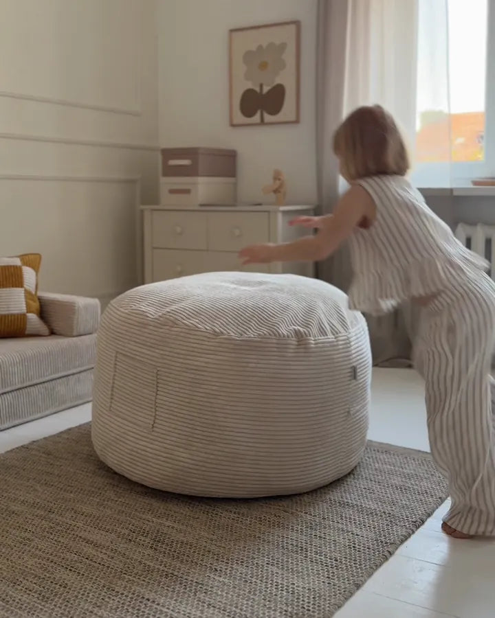 Uśmiechnięta dziewczynka leży na pufie Futon, obok maskotka w kieszeni.
