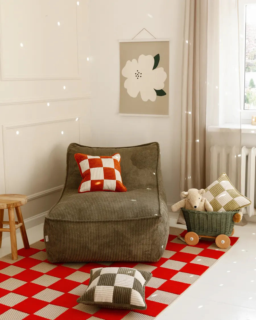 Kumo Lounger w kolorze Dusty Sage w pokoju dziecięcym, na dywanie w czerwono-białą kratę