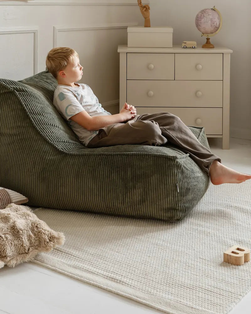 Chłopiec wygodnie leży w Kumo Lounger, w kadrze cały fotel i pokój